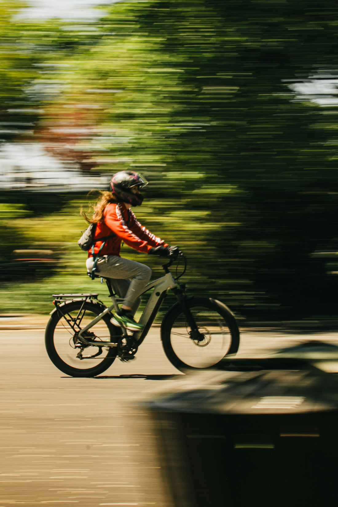 Cyclist in red jacket rides fast with blurred green trees